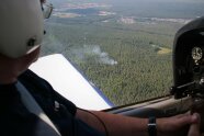 Mann mit Helm blickt aus Flugzeugfenster auf Waldbestand