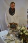 Frau hinter dekoriertem Tisch, Gesteck mit weißen Rosen, Menütafel, Kerze, Geschirr gefalteter Serviette, Besteck, Gläser