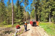 Feuerwehrmann vor Pumpe und Gerätewagen im Wald