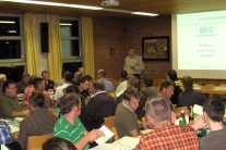 Foto mehrerer Zuhörer und eines Vortragenden vor einer Leinwand mit Präsentation